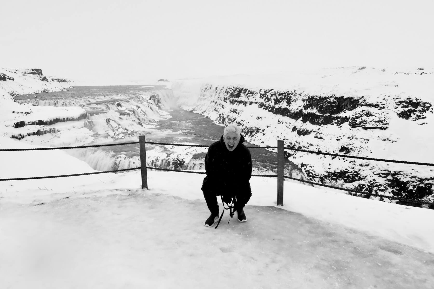 A man kneeling down on the snow near a fence.