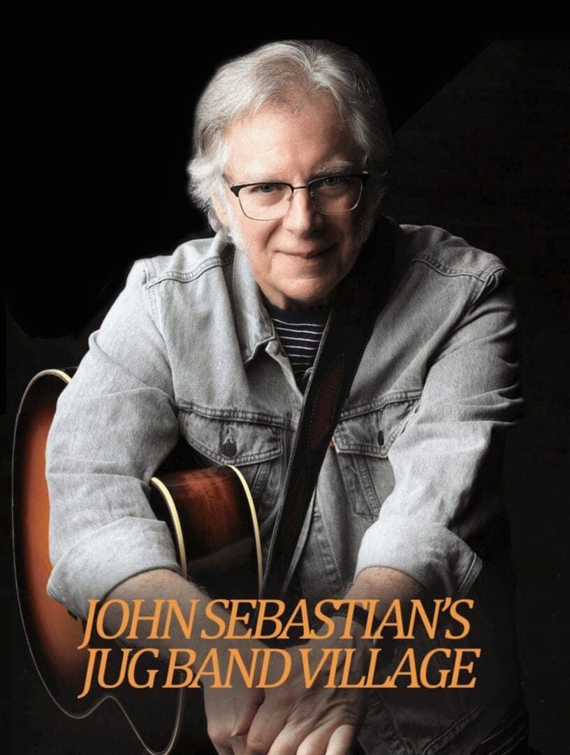 A man sitting in front of an acoustic guitar.